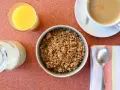 Miseczka pełna granoli, szklanka soku pomarańczowego, mleko i kawa. Czy granola jest zdrowa? Zależy od składników!