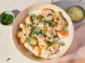 Pyszne gnocchi z łososiem w kremowym sosie, udekorowane koperkiem i kaparami. Obok miseczka z tartym serem.