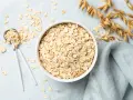 Misternie ułożone płatki owsiane w misce i na łyżce. Czy płatki owsiane mają gluten? Zależy od sposobu przetworzenia.