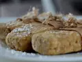 Domowe batony proteinowe przepis. Trzy domowe batony proteinowe, posypane wiórkami kokosowymi, zawinięte w papier i związane sznurkiem.