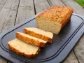 Chleb z mąki kokosowej, pokrojony na kromki, leży na czarnej desce na drewnianym stole.