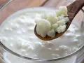 Drewniana łyżka z grzybkiem tybetańskim nad szklanką pełną mlecznego napoju.