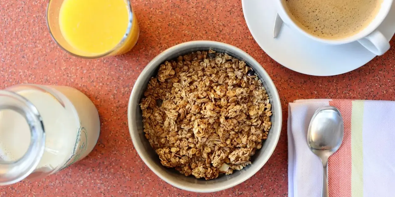 Miseczka pełna granoli, szklanka soku pomarańczowego, mleko i kawa. Czy granola jest zdrowa? Zależy od składników!