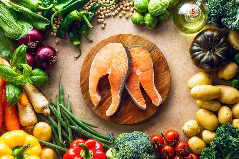 Dwa soczyste steki z łososia na desce, otoczone świeżymi warzywami i ziołami. Idealna dzienna dawka omega 3 dla zdrowia.
