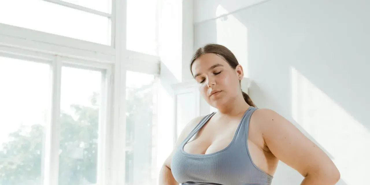 Kobieta w sportowym topie zamyka oczy, zastanawiając się nad zdrowym odżywianiem. Dieta przy endometriozie może przynieść ulgę.