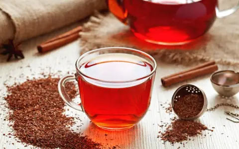 Czerwona herbata rooibos, znana ze swoich właściwości zdrowotnych, w szklanej filiżance, obok cynamonu i gwiazdki anyżu.