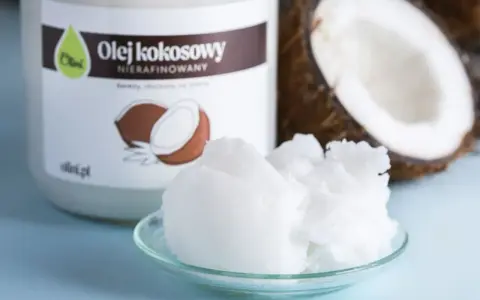 Olej kokosowy nierafinowany na talerzyku, obok słoika i połówki kokosa. Idealny jako olej do smażenia.