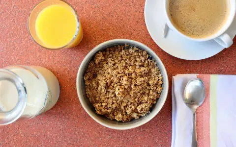 Miseczka pełna granoli, szklanka soku pomarańczowego, mleko i kawa. Czy granola jest zdrowa? Zależy od składników!