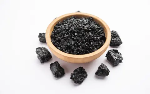 Czarna, grudkowata substancja w drewnianej miseczce i wokół niej. To shilajit, znany ze swoich właściwości.