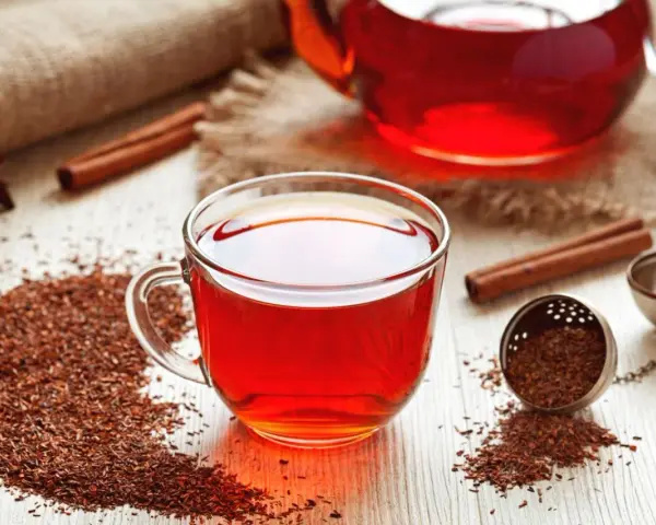 Czerwona herbata rooibos, znana ze swoich właściwości zdrowotnych, w szklanej filiżance, obok cynamonu i gwiazdki anyżu.