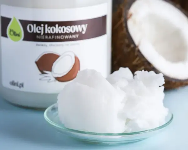Olej kokosowy nierafinowany na talerzyku, obok słoika i połówki kokosa. Idealny jako olej do smażenia.