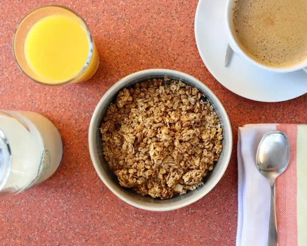 Miseczka pełna granoli, szklanka soku pomarańczowego, mleko i kawa. Czy granola jest zdrowa? Zależy od składników!