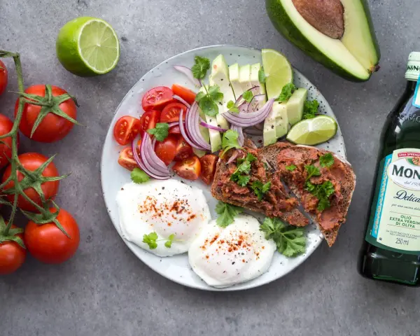 Śniadanie idealne na dietę 1500 kcal: jajka sadzone, tost z pastą, awokado, pomidorki, cebula i limonka.