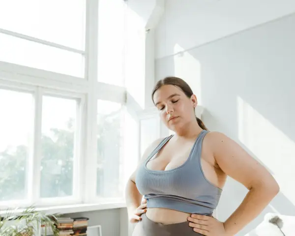 Kobieta w sportowym topie zamyka oczy, zastanawiając się nad zdrowym odżywianiem. Dieta przy endometriozie może przynieść ulgę.