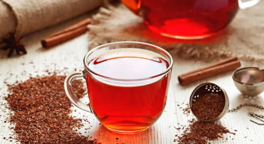Czerwona herbata rooibos, znana ze swoich właściwości zdrowotnych, w szklanej filiżance, obok cynamonu i gwiazdki anyżu.