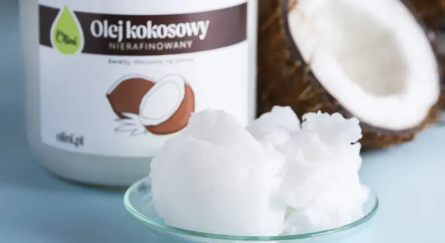 Olej kokosowy nierafinowany na talerzyku, obok słoika i połówki kokosa. Idealny jako olej do smażenia.
