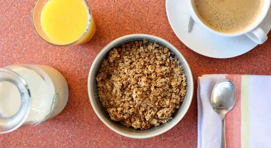 Miseczka pełna granoli, szklanka soku pomarańczowego, mleko i kawa. Czy granola jest zdrowa? Zależy od składników!