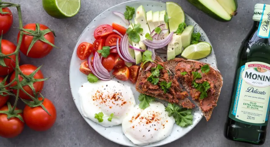 Śniadanie idealne na dietę 1500 kcal: jajka sadzone, tost z pastą, awokado, pomidorki, cebula i limonka.