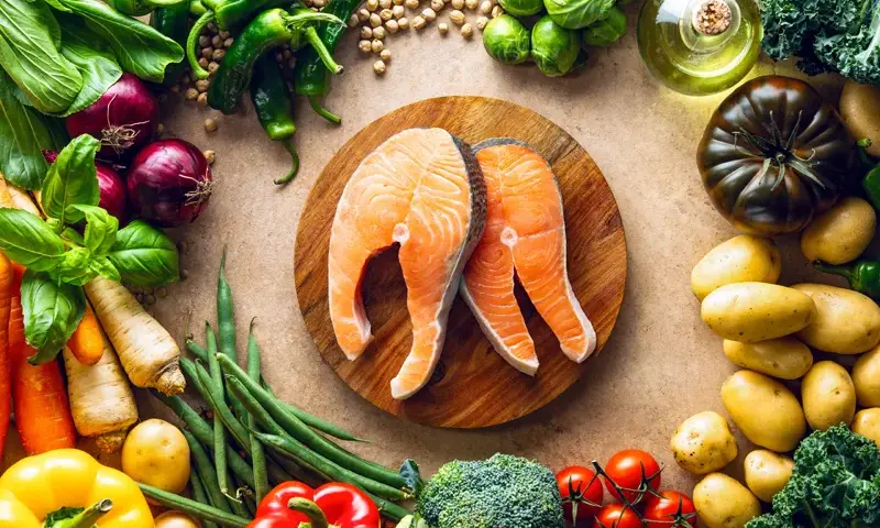 Dwa soczyste steki z łososia na desce, otoczone świeżymi warzywami i ziołami. Idealna dzienna dawka omega 3 dla zdrowia.