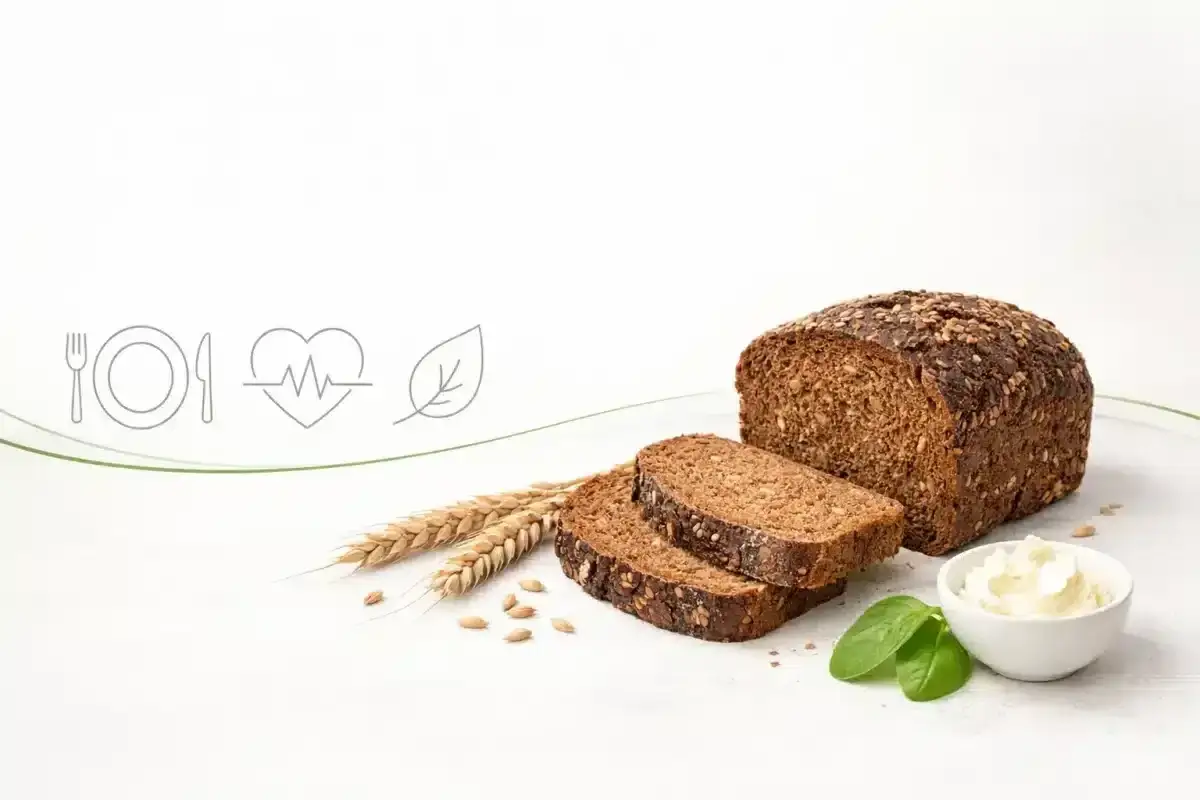Pełnoziarniste pieczywo na diecie to zdrowy wybór. Na zdjęciu bochenek, kromki, kłosy, nasiona i serek.