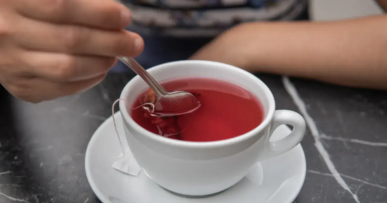 Ręka miesza łyżeczką czerwony napar z hibiskusa. Czy to działanie niepożądane?