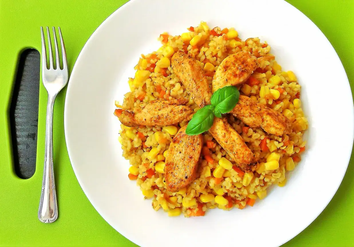 Pyszna kasza bulgur z kurczakiem, kukurydzą i marchewką, ozdobiona listkiem bazylii. Idealny obiad!