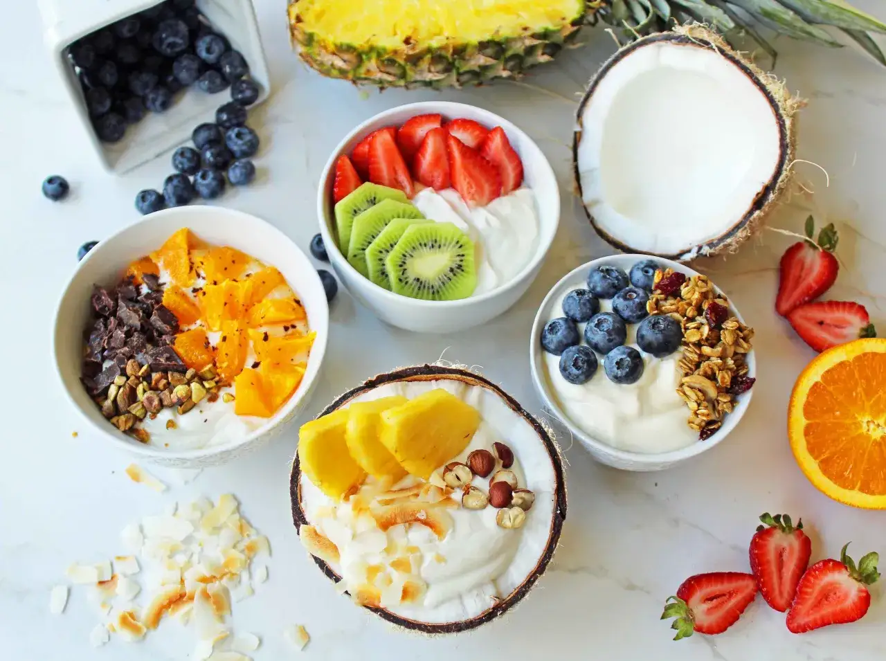 Kolorowe miseczki z jogurtem i owocami: jagody, truskawki, kiwi, pomarańcze, ananas, kokos, orzechy i granola. Idealne zdrowe przekąski na każdy dzień.