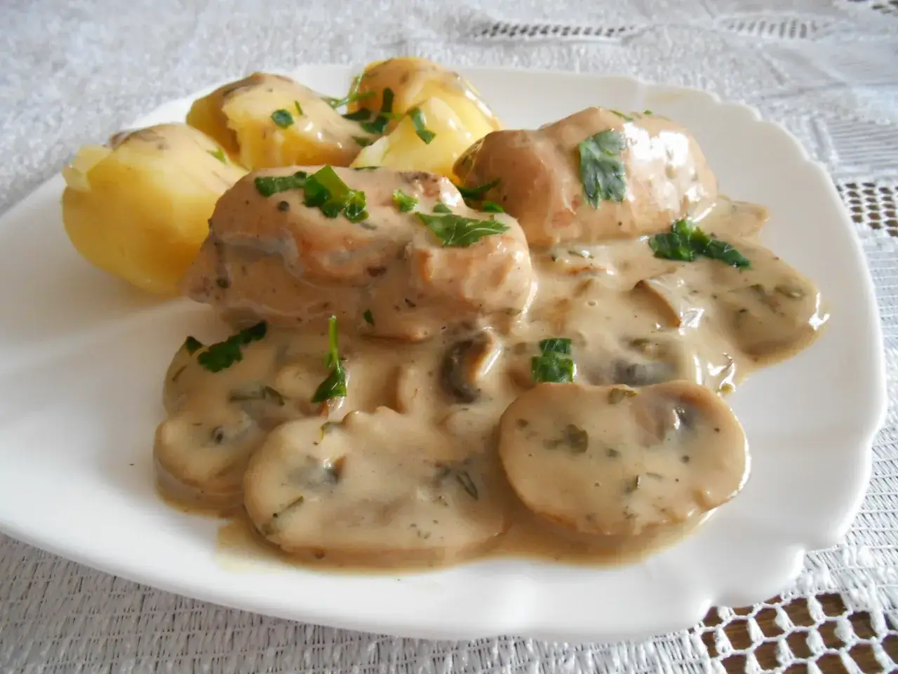 Pyszny kurczak w sosie grzybowym z ziemniakami, posypany świeżą natką pietruszki.